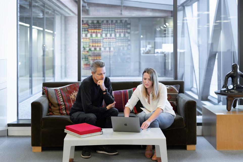 man and woman sitting on couch using macbook